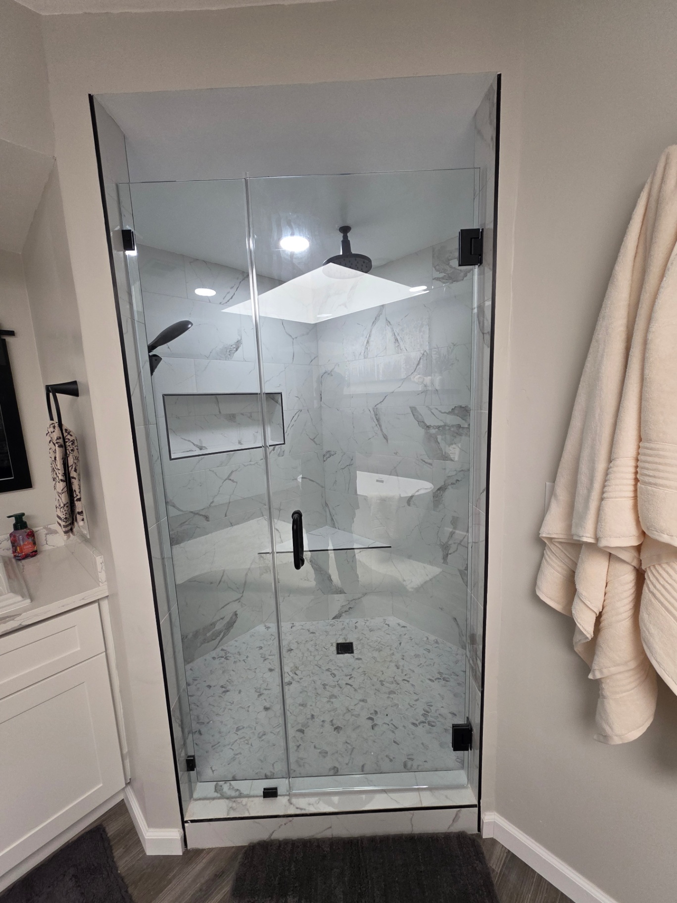 Custom walk-in marble shower with frameless glass, rainfall head, and pebble mosaic floor