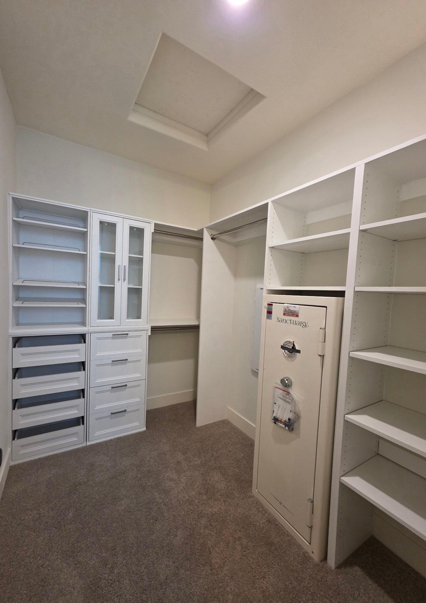 Custom walk-in closet build with white cabinetry, glass display doors, and tray ceiling detail